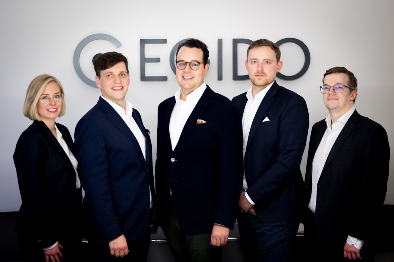 Fünf EGIDO-Mitarbeiter stehen in formeller Kleidung vor einem neutralen Hintergrund mit dem Schriftzug 